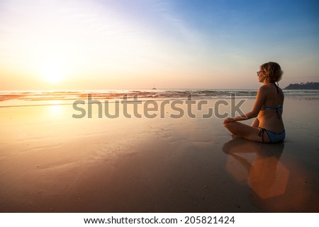 Yoga woman sitting on sea coast at beautiful sunset.