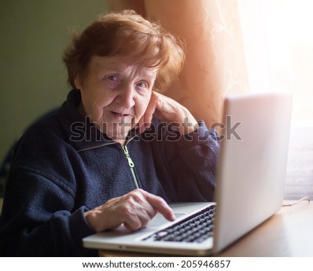Elderly woman sing laptop computer at home.