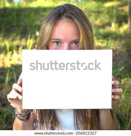 Girl holding clean white sheet paper, in the park (banner for message)