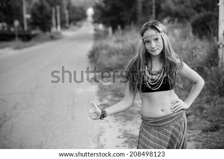 Young lovely hippie girl hitch hiking on countryside road (black and white photo)
