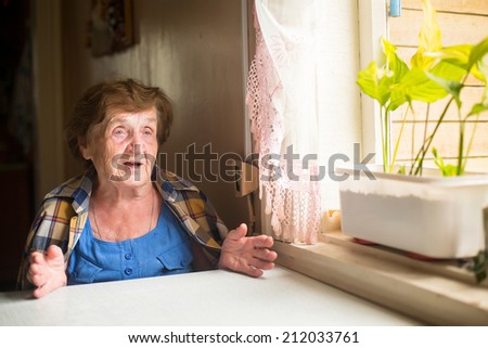 Elderly woman sitting at table and talk in his house.