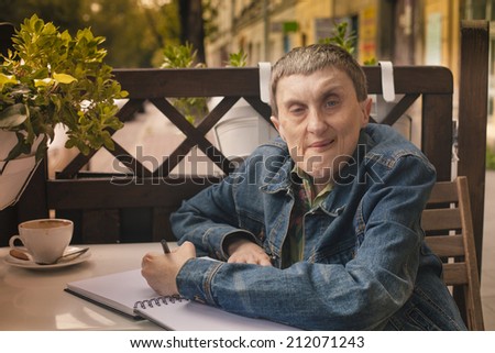 Disabled man with cerebral palsy writing in a notebook sitting at an outdoor cafe.
