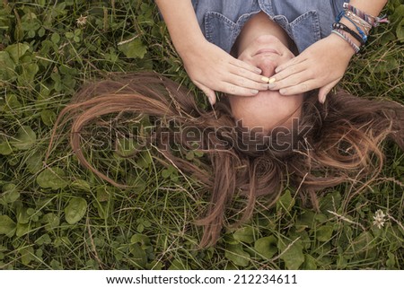 Young girl covers his eyes with his hands lying on the grass, top view.