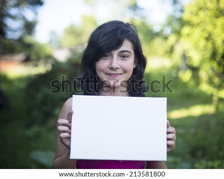 Young girl holding clean white sheet paper, outdoors (for your message)