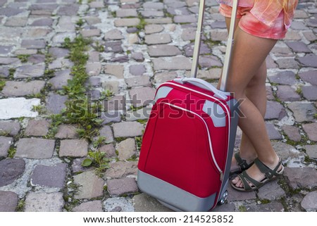 Travel concept. Red suitcase and legs of a young girl on the cobbles road.