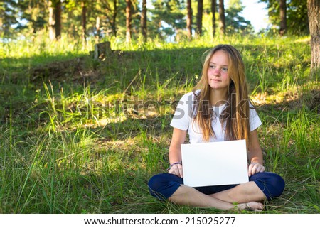 Young pretty girl sitting on the nature of holding a white banner.