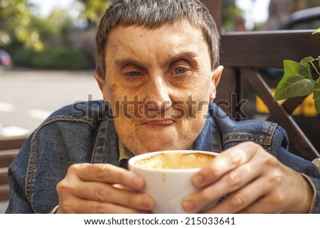 Closeup portrait of elderly disabled man with cerebral palsy, at an outdoor cafe.