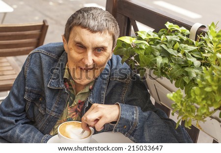 Elderly disabled man with cerebral palsy, smiling sitting at an outdoor cafe.