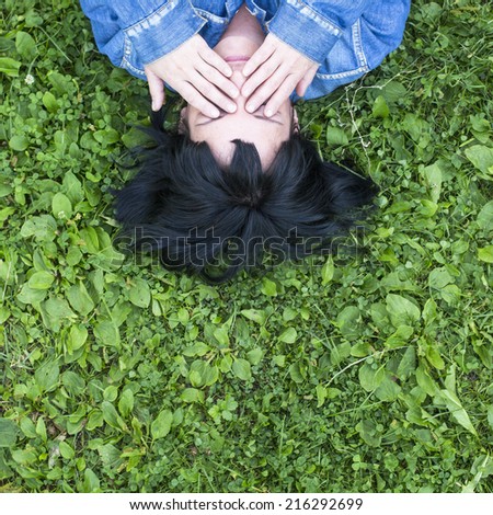 Young woman lying on the grass covers his eyes with his hands, top view with space for text.