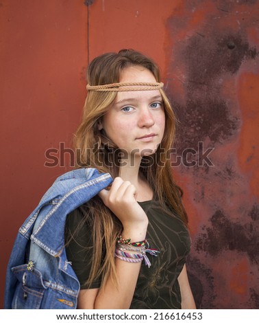 Young beautiful girl dressed in hippie style, against a background of burgundy metal wall.