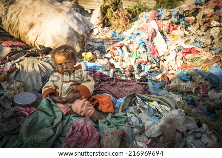 KATHMANDU, NEPAL - DEC 22, 2013: Unidentified child is sitting while her parents are working on dump. In Nepal annually die 50,000 children, in 60% of cases - malnutrition.