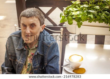 Disabled man with cerebral palsy, smiling sitting at an outdoor cafe.