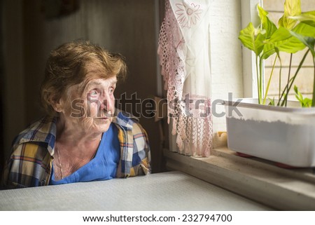 Old woman sitting alone near the window in his house. Loneliness in old age.