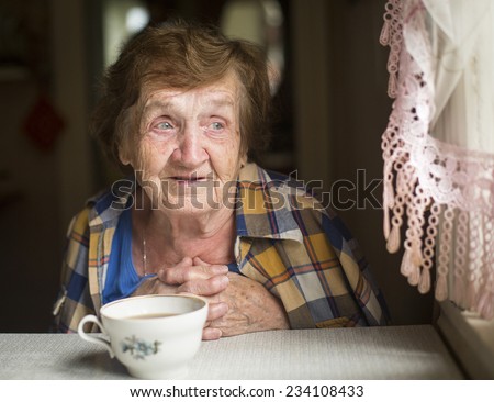 Old woman sitting alone near the window in his house.