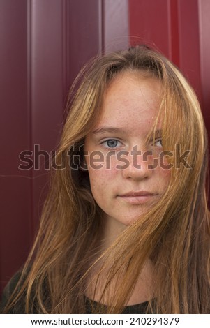 Close-up portrait of a young pretty girl on a background of metallic red wall.