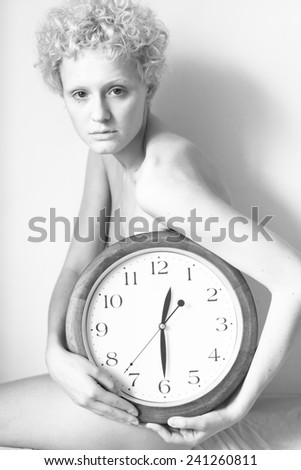 Young cute naked girl with curly hair holding a big clock. Black and white photography.