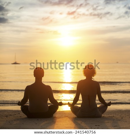 Young yoga couple is meditating in the Lotus position on the sea beach during sunset.