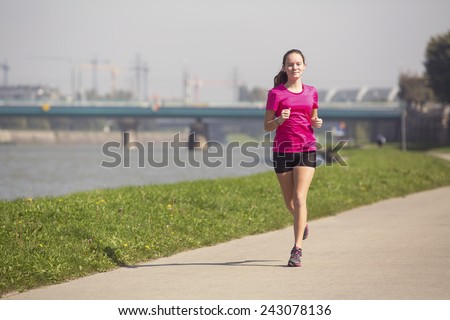 Young girl runs on Jogging track along the river in a big city. A healthy way of life.