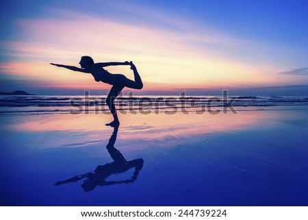 Silhouette of woman with reflection, doing exercises on the beach during sunset.