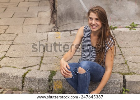 Young cute hipster girl sitting on curb on the street in old town.