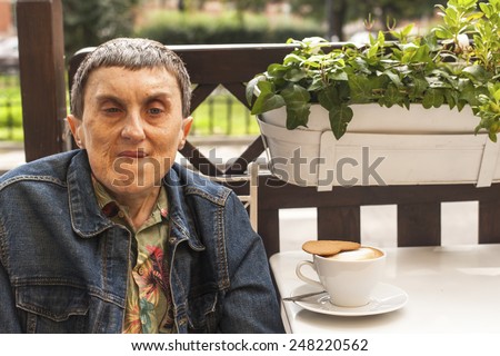 Portrait of disabled man with cerebral palsy sitting at outdoor cafe with a cup of coffee.