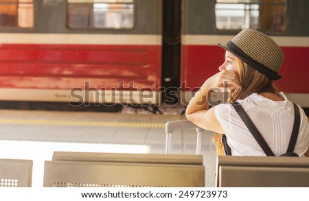 Young cute girl waiting for the train at the railway station. Travel concept.