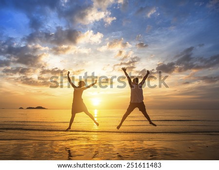 Couple in love to jump up on the beach during a stunning sunset.