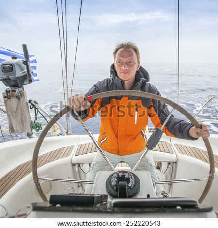 Young man Skipper early in the morning at the helm of a yacht in the open sea.
