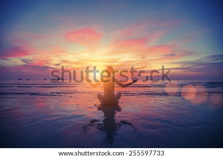 Woman doing meditation near the ocean beach. Yoga silhouette.