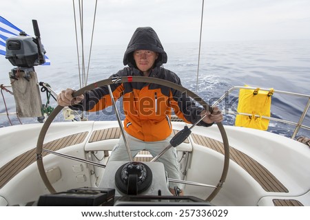 Young man skipper in the sea at the helm of a sailing yacht.