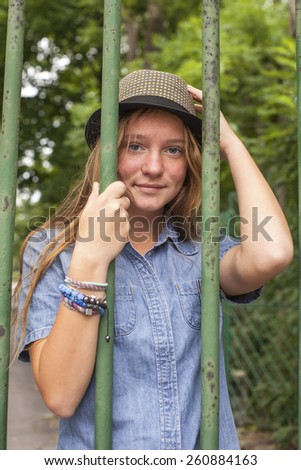 A pretty young girl standing behind bars in the city Park.