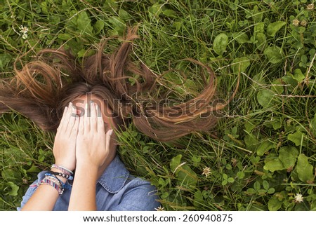 Girl lying on the grass with scattered hair covers his face with his hands.
