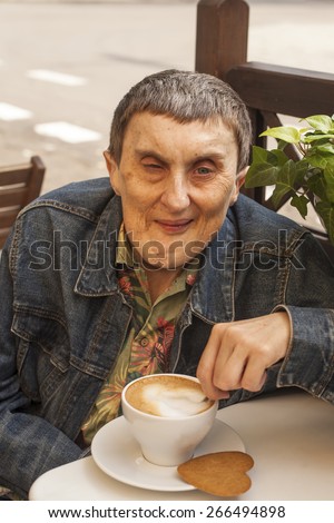 Elderly disabled man with cerebral palsy sitting at outdoor cafe with cup of coffee.