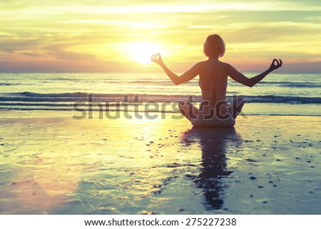 Silhouette of woman at yoga pose on the beach during an amazing sunset.