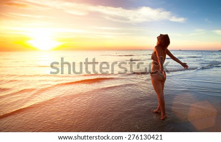Young beautiful woman stands towards the sun on Sea beach during a amazing sunset.