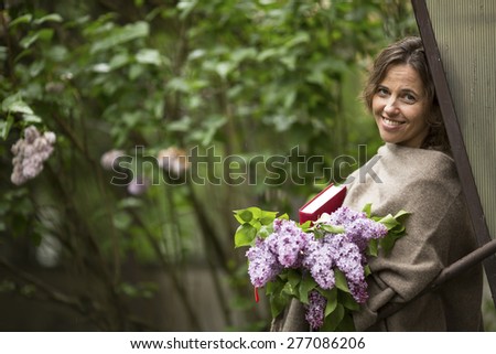 Beautiful woman with a bouquet of lilacs and a book in his hands, in the open air among the greenery.