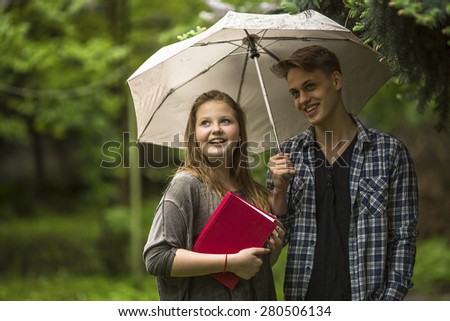 Young couple in the Park under an umbrella, a girl holds a red book in his hands.