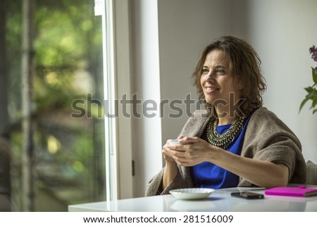 Woman sits in front of the window with a Cup of tea.