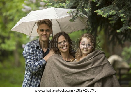 Woman with their adult children, daughter and son, in the Park under an umbrella.