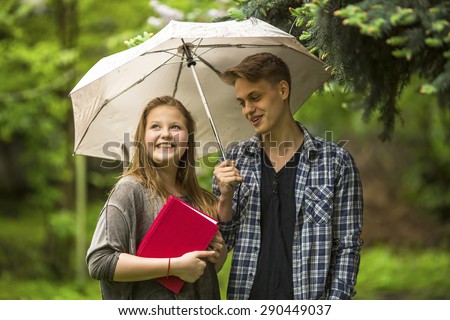 Girl with a red book in his hands and the guy with the umbrella outdoors. A couple of students talking.