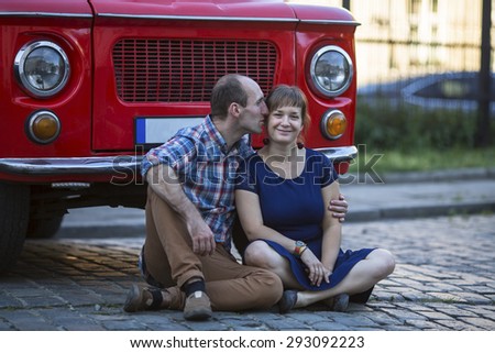 Happy young family. Couple in love sitting on the pavement near a vintage seventies style car.