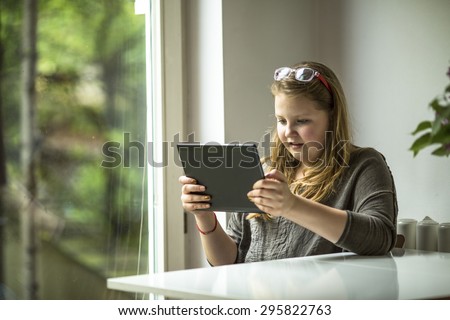 Teen girl sitting with a tablet near the window in house.