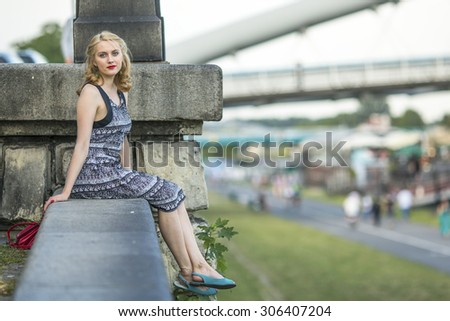 Beautiful blond lady sitting on a stone embankment.