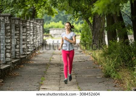 Young woman running on the track through the summer park. Training outdoors. Workout in a Park.