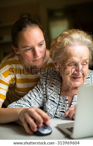 Young girl teaches elderly woman working on the computer. Granddaughter with her grandmother near the computer.
