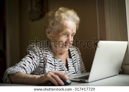 Old woman sitting with laptop at table in his house.