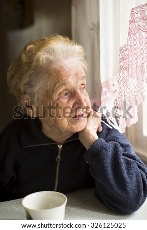 An elderly lady sitting near the window in the kitchen.