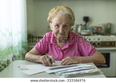 An elderly woman fills the bill for utilities sitting at the table in the kitchen.