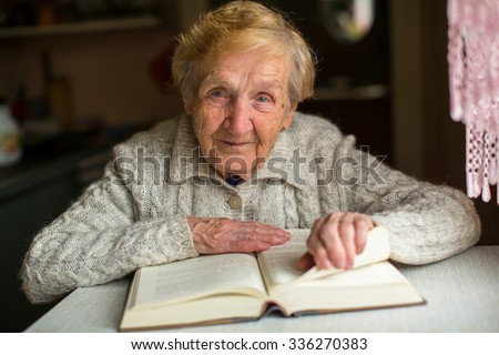 Old woman reading a book sitting at the table.