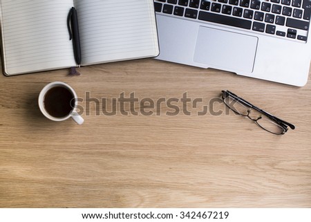 Notepad with pen, keyboard of laptop, glasses and coffee Cup on wooden table top. Top view with space for your text.